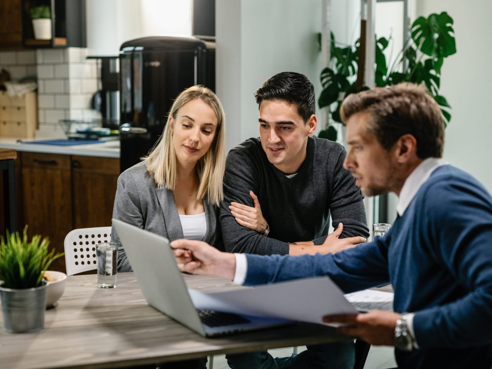 Young couple and real estate agent using laptop while going through housing plan on a meeting.